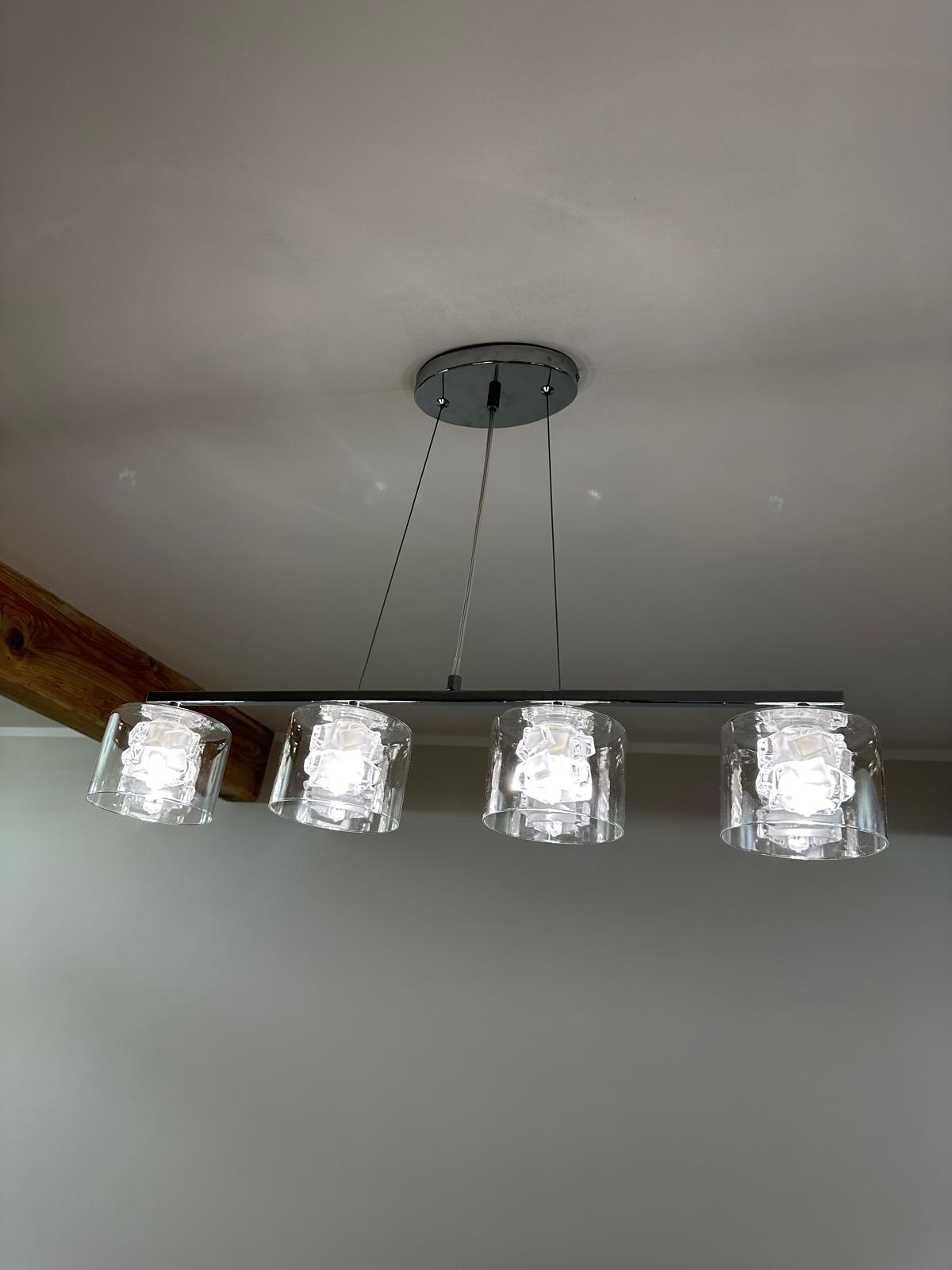 Four-shade linear glass pendant installed over a dining space, level and balanced.