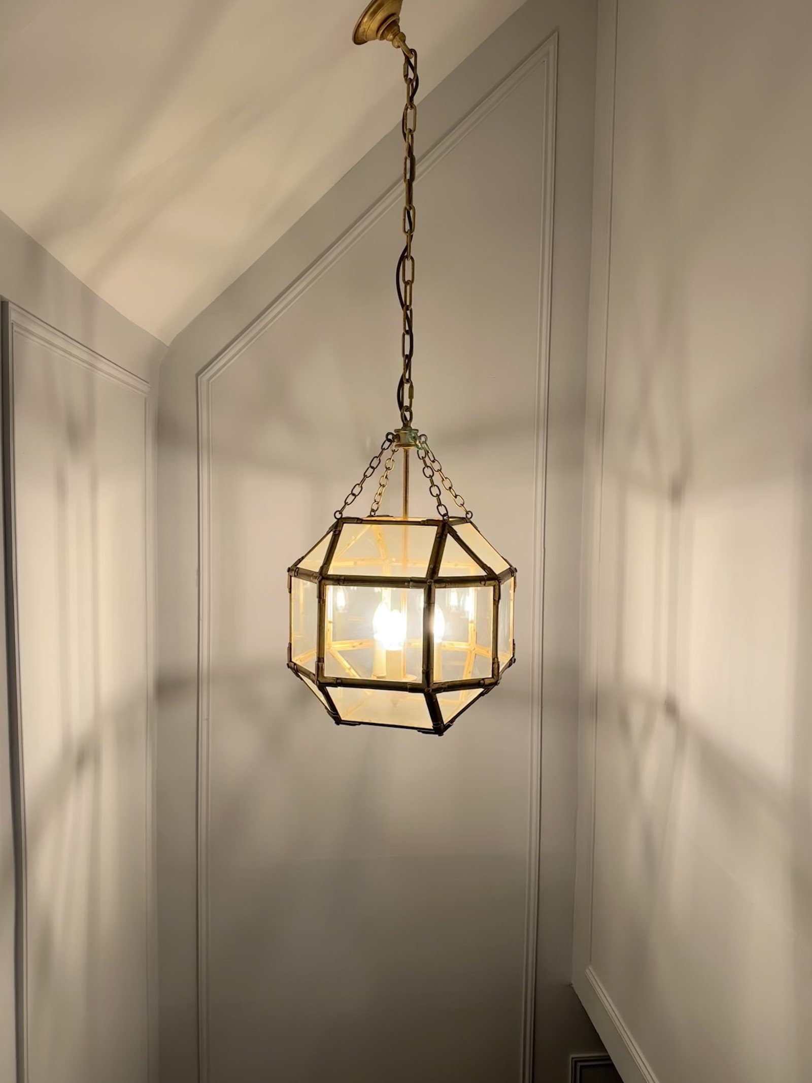 Brass-and-glass lantern pendant hung in a panelled hallway, chain dressed and centred.
